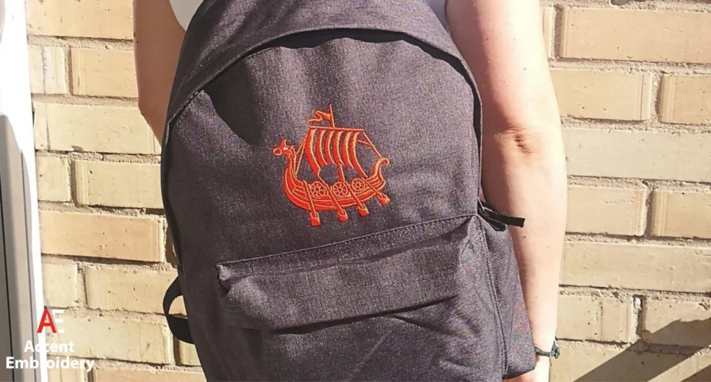 A woman holds a backpack featuring a boat design, showcasing custom embroidery on the fabric.