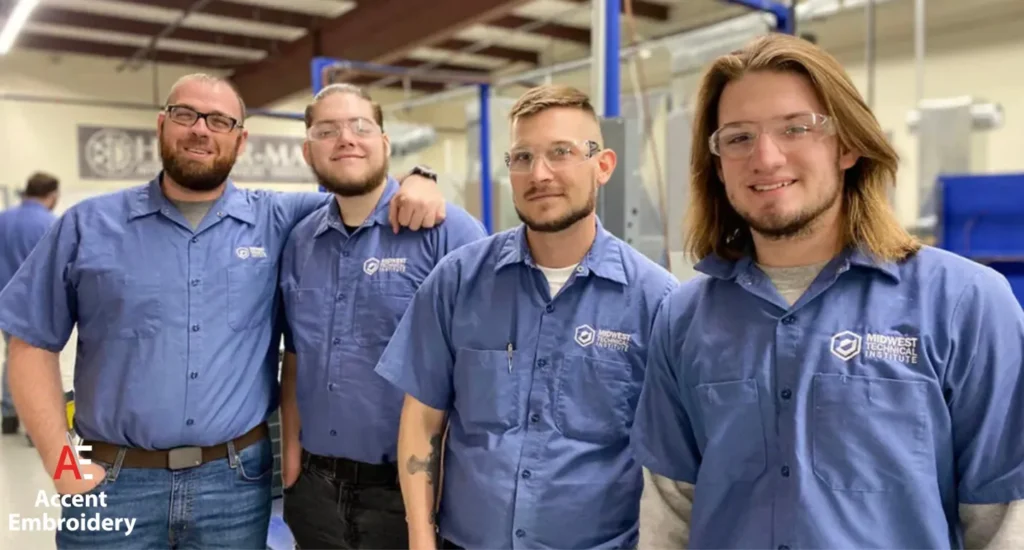 Four men in blue shirts stand together inside a factory, engaged in a discussion about their work.